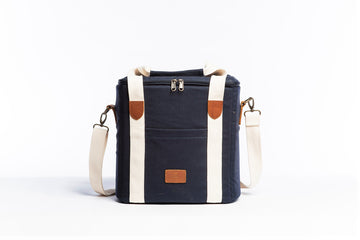 Front on image of the Slowlife Collection Navy Cooler Bag. This has a front pocket, leather detailing and a long shoulder strap included.