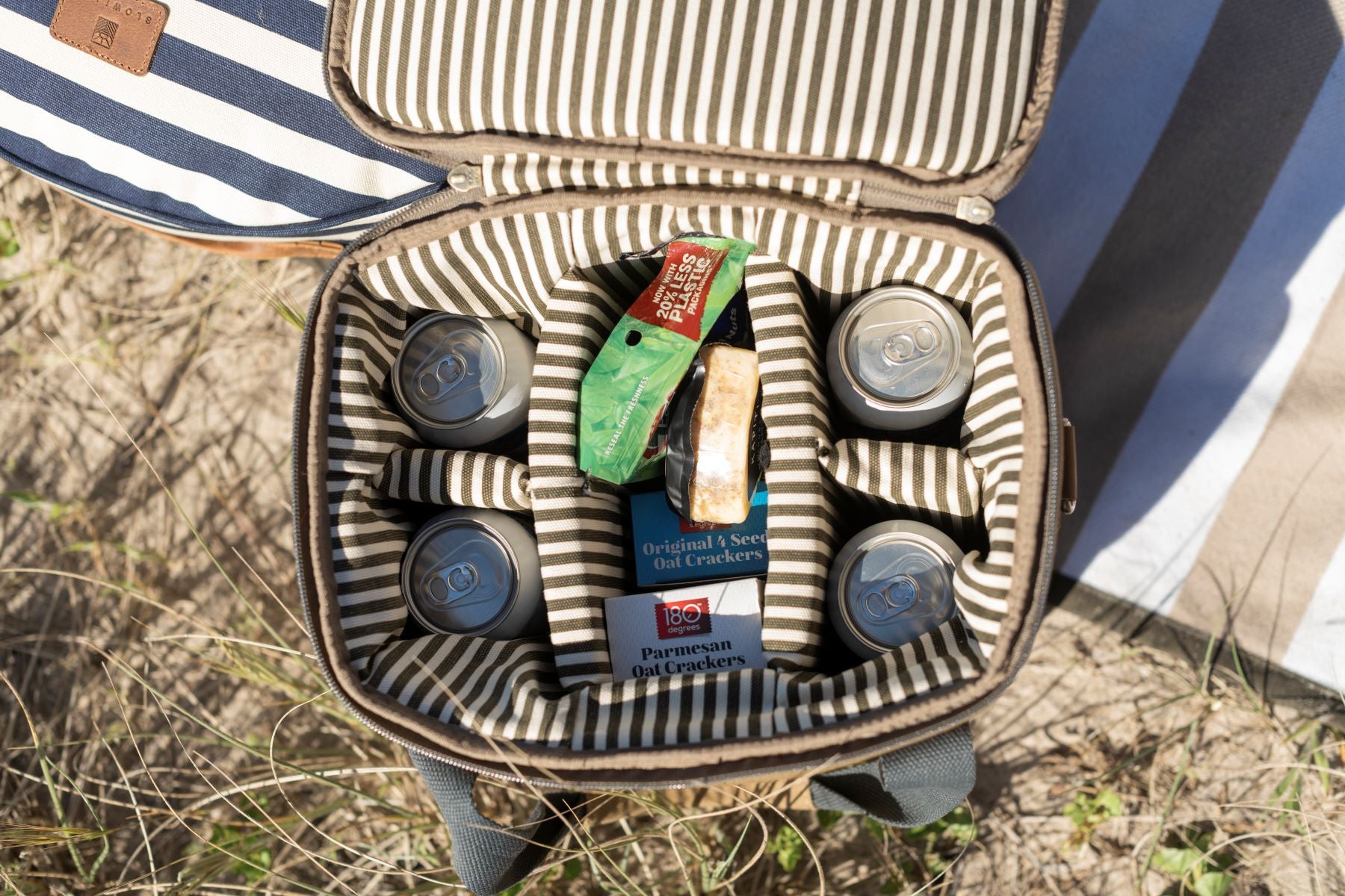 Birds eye view of the Olive Cooler Bag interior. Striped olive lining with dividers for drinks and food. The cooler bag is full of cans and food.