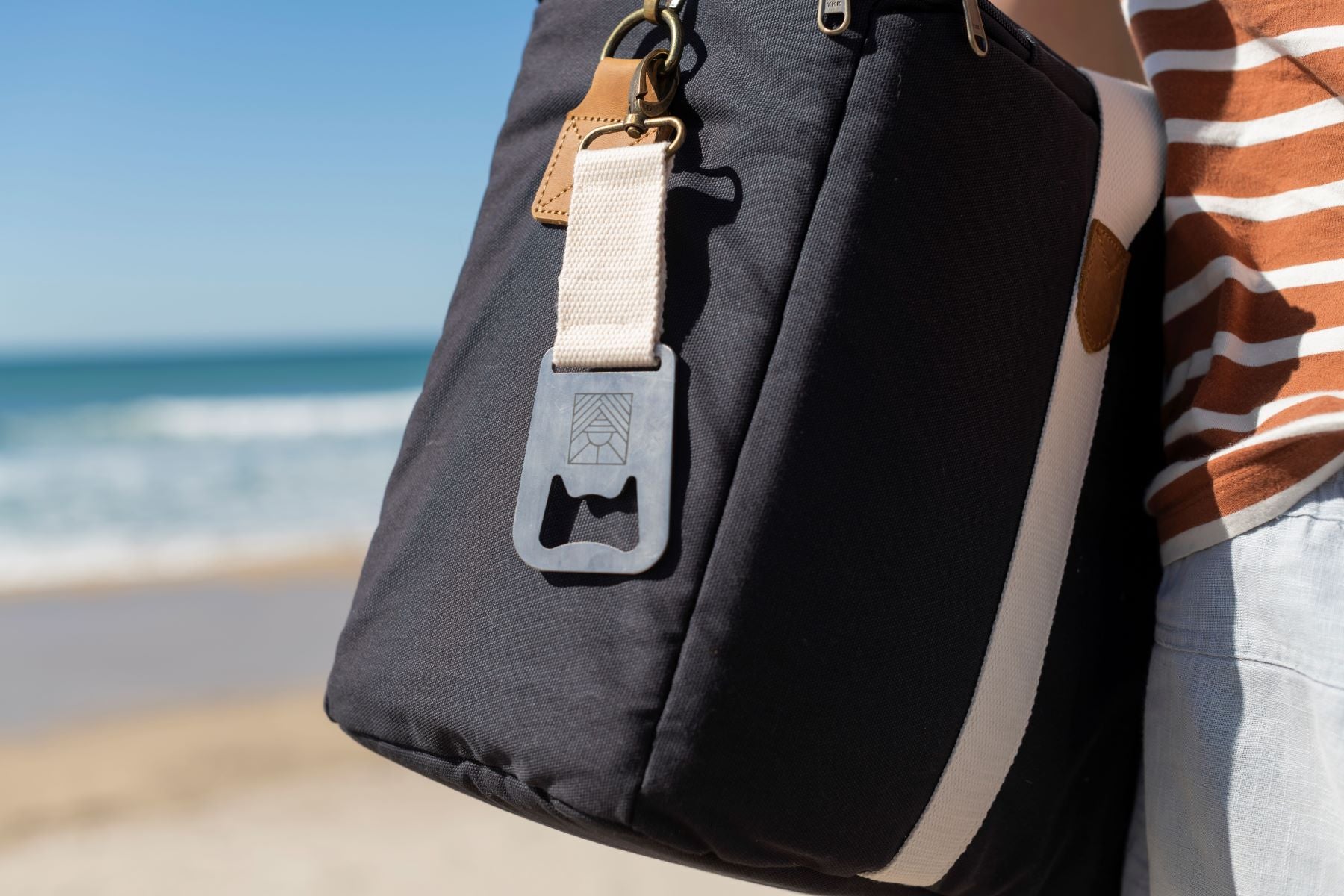 Navy Slowlife Collection Picnic Bag with a white Slowlife Collection Bottle Opener clicked onto the handle.