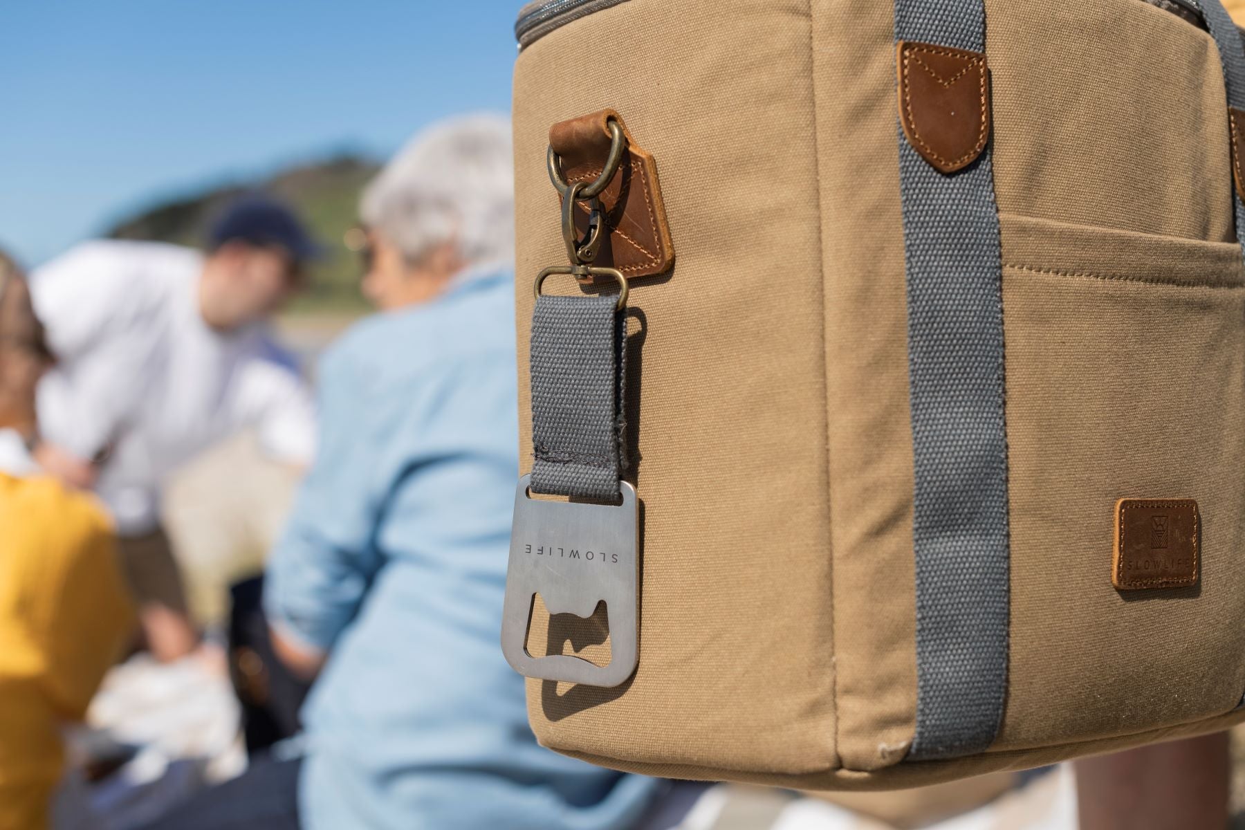 Olive Slowlife Collection Picnic Bag with a grey Slowlife Collection Bottle Opener clicked onto the handle.