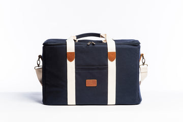 A front on photo of the Slowlife Collection Picnic Bag. Showing the cream straps with leather detailing, a front pocket and shoulder strap attached.