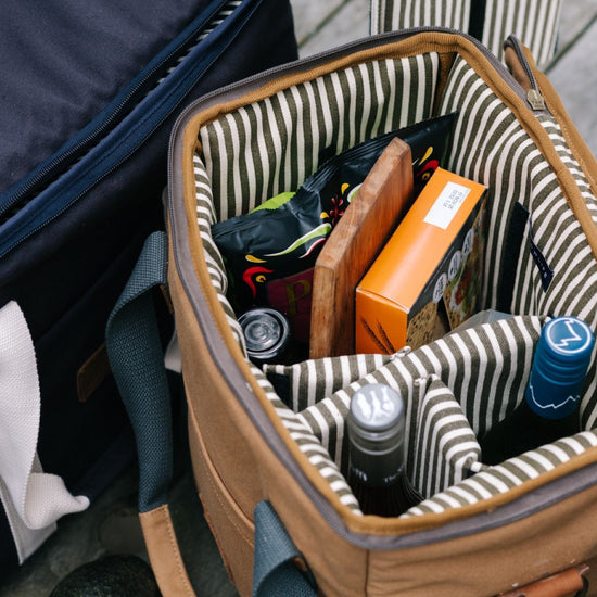 Tan cooler bag with striped interior, packed with wine and snacks.