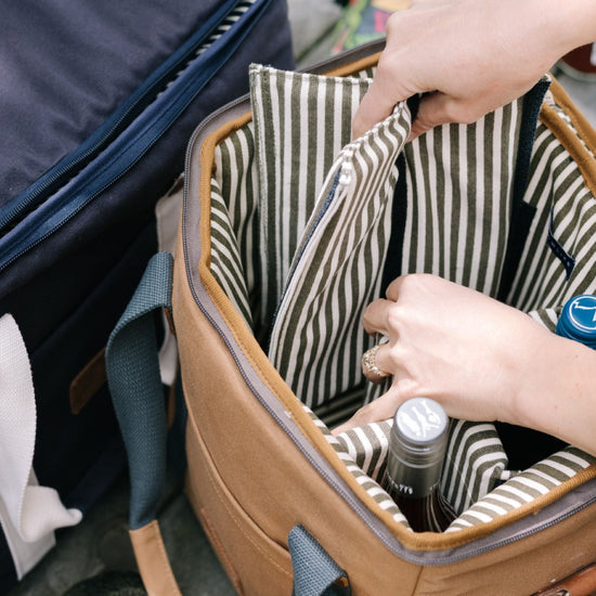 Hands packing bottles into a striped-interior cooler bag.
