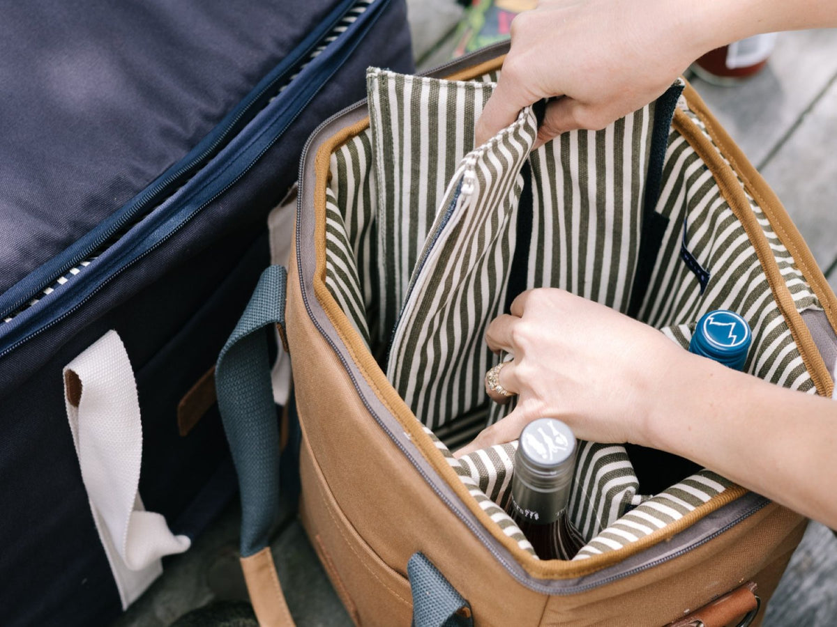 Hands packing bottles into a striped-interior cooler bag.