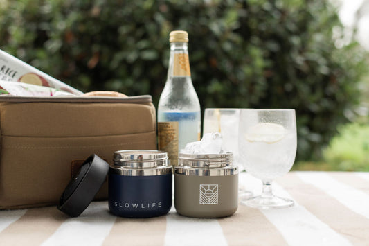 The Navy & Olive Slowlife Collection 8oz Flask on the Slowlife Collection picnic rug with the Olive Slowlife Collection Lunch Bag, a couple of drinks and a bottle of tonic.