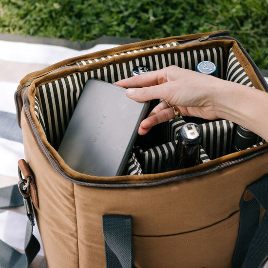 Person reaching into a striped picnic basket with a plate.