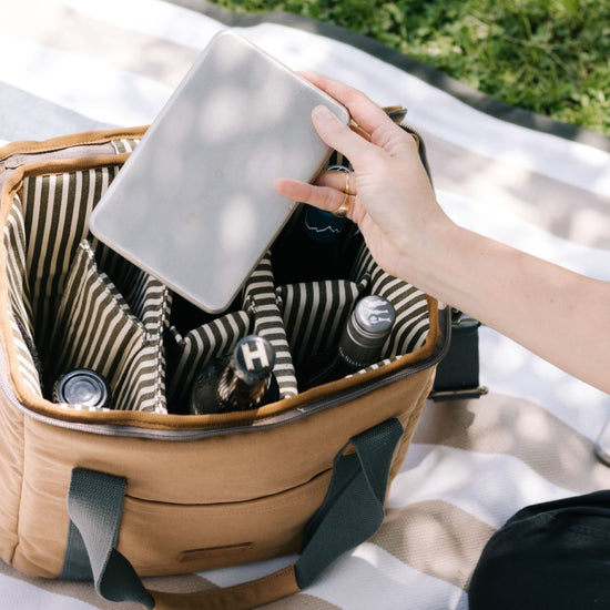 Person reaching into a beige picnic basket, holding a plate.