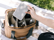Person reaching into a beige picnic basket, holding a plate.