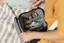 Hand packing snacks and cans into a striped cooler bag.