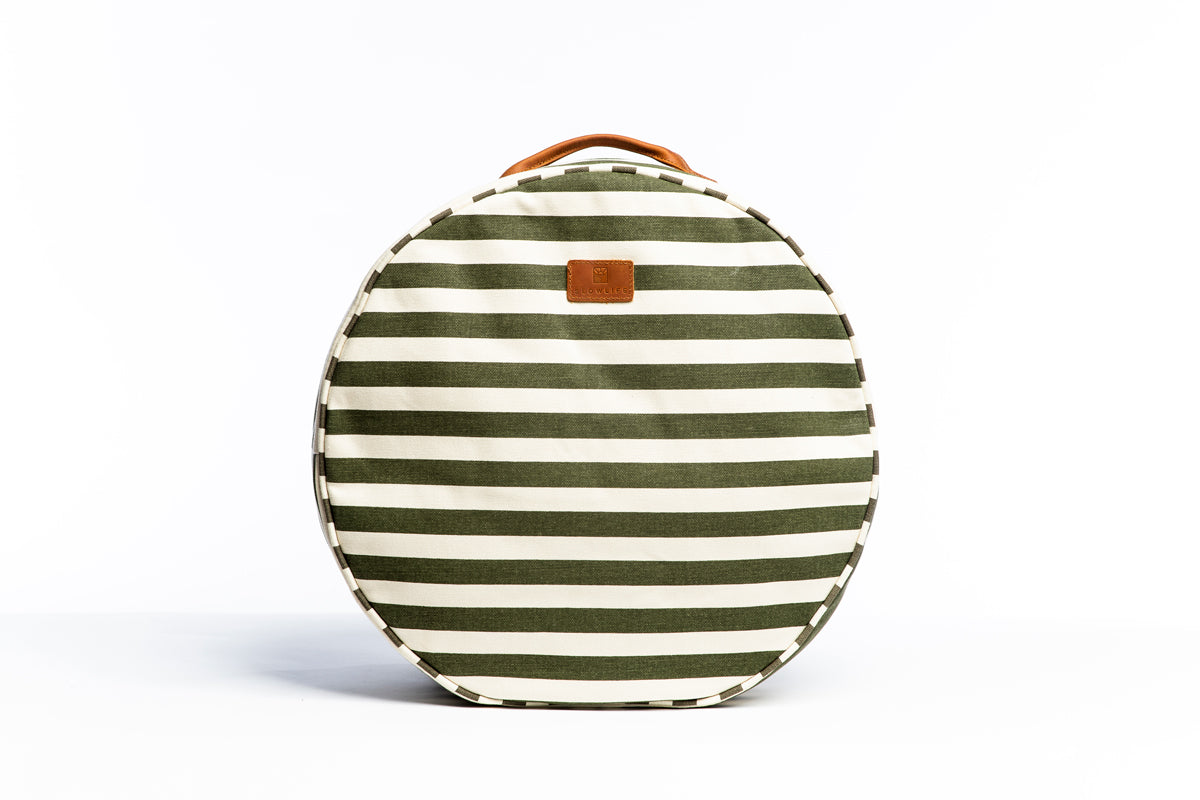 A front on photo of the Olive and cream striped Slowlife Collection cushion. Showing the leather handle and branded patch.
