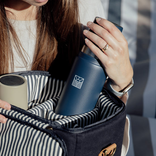 Person holding a striped cooler bag with a blue thermos inside, blurred background