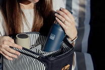 Person holding a striped cooler bag with a blue thermos inside, blurred background